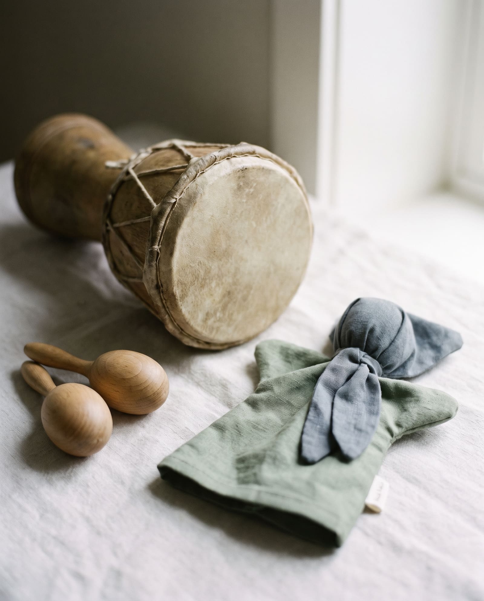 A small hand drum, wooden shakers and a plain cloth puppet on a linen cloth